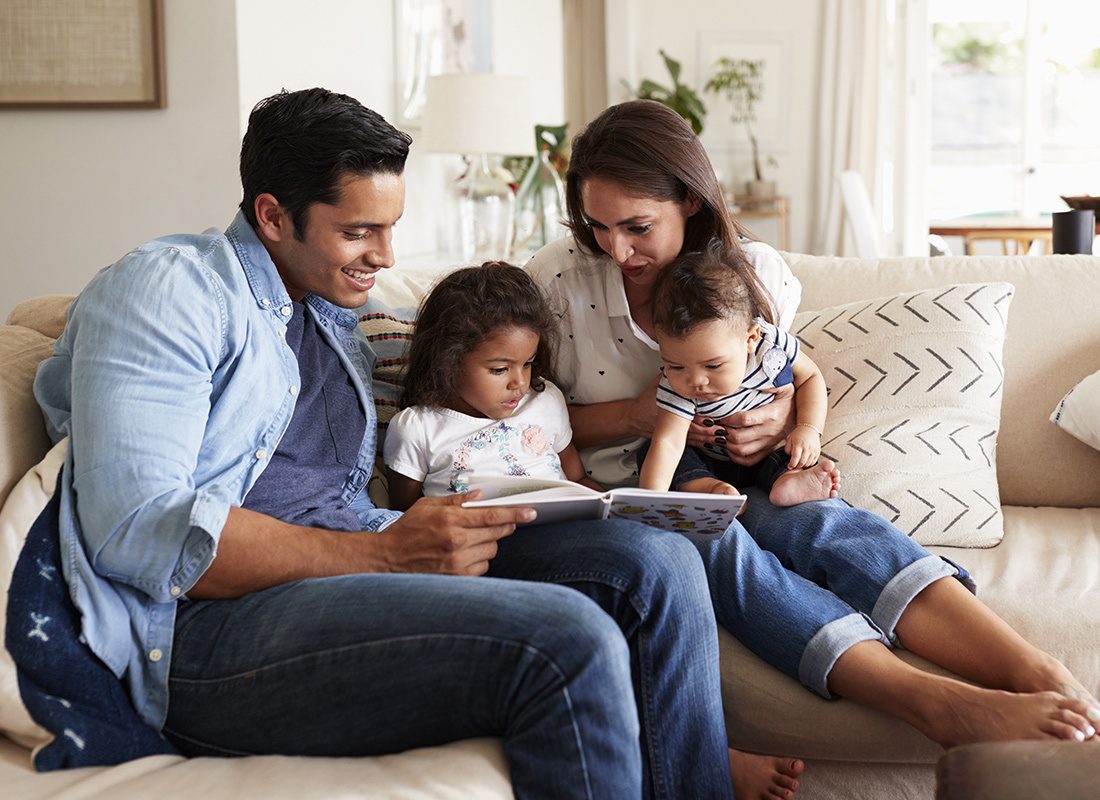 Insurance Solutions - Young Family Sitting Close On Their Couch Reading a Book